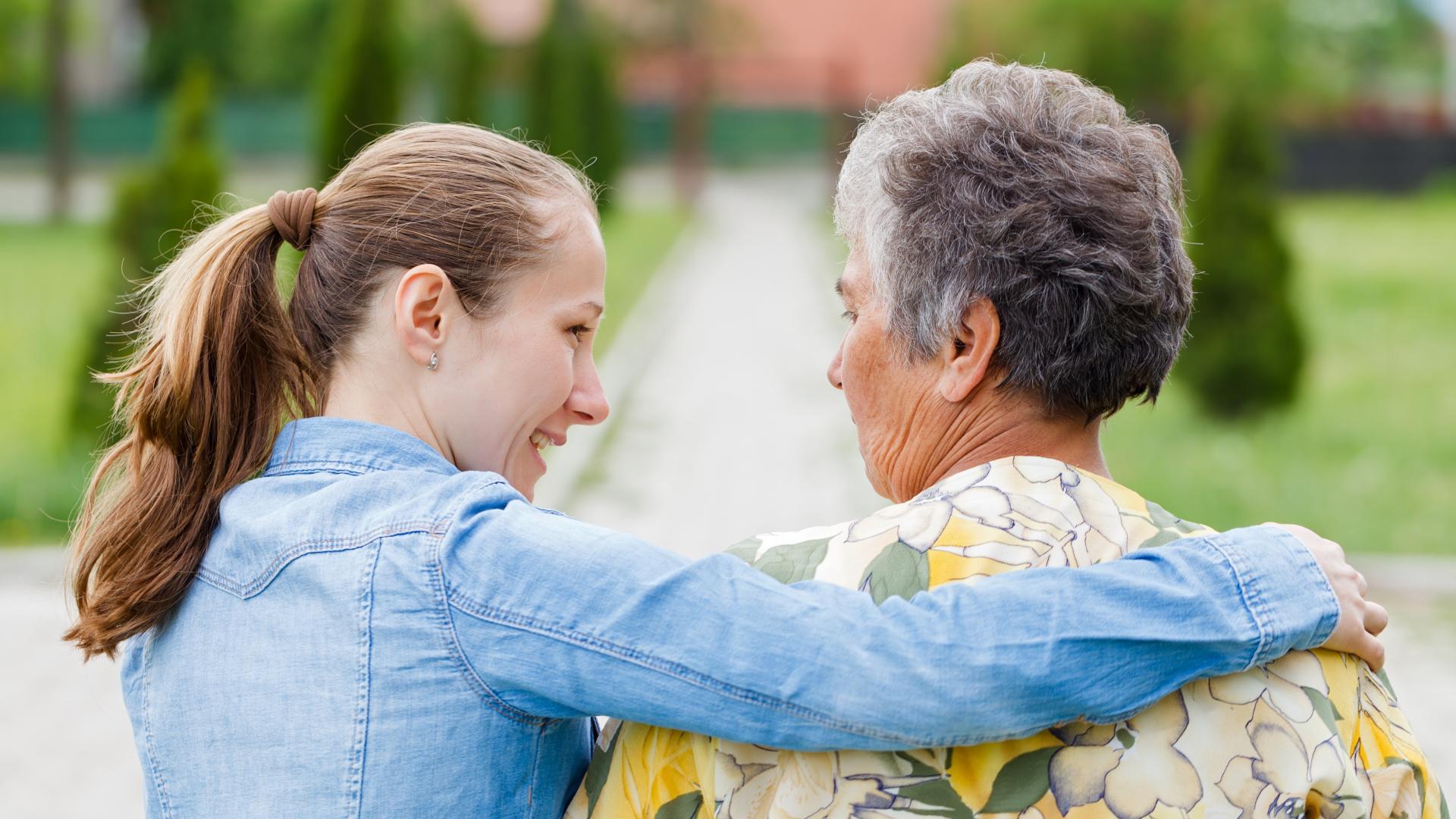 Jonge vrouw met arm om schouders van demente vrouw